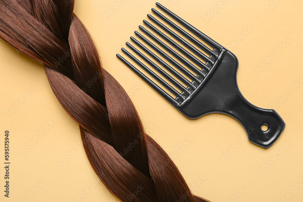 Braided hair strand with brush on beige background, closeup