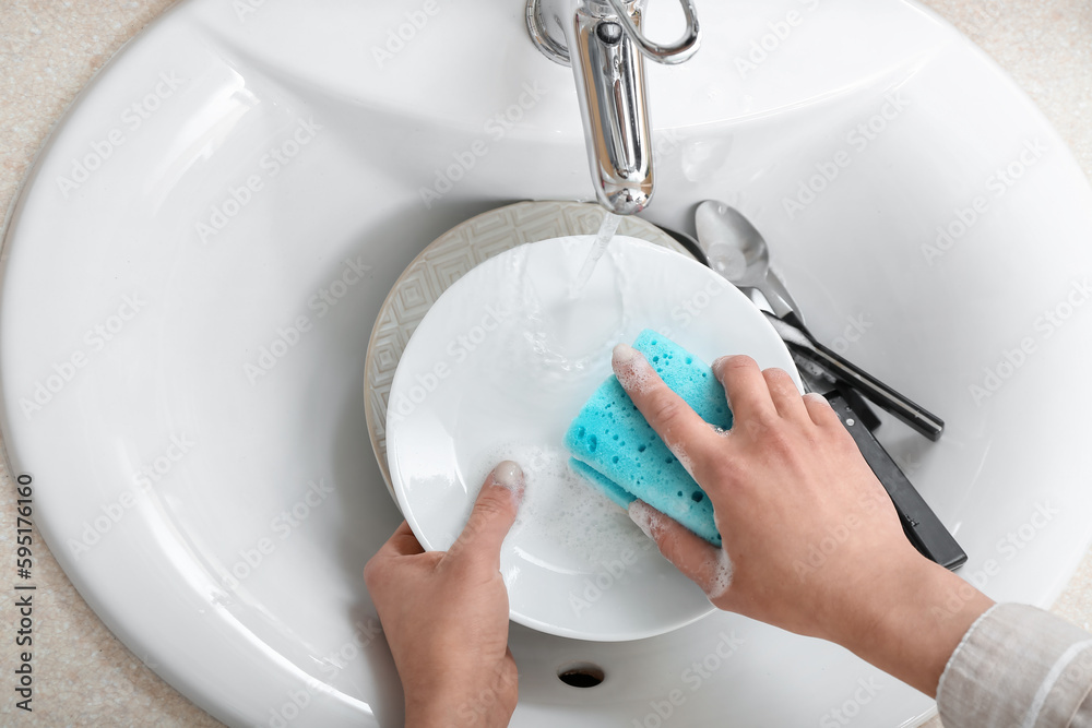 Woman washing plate with sponge in sink, closeup