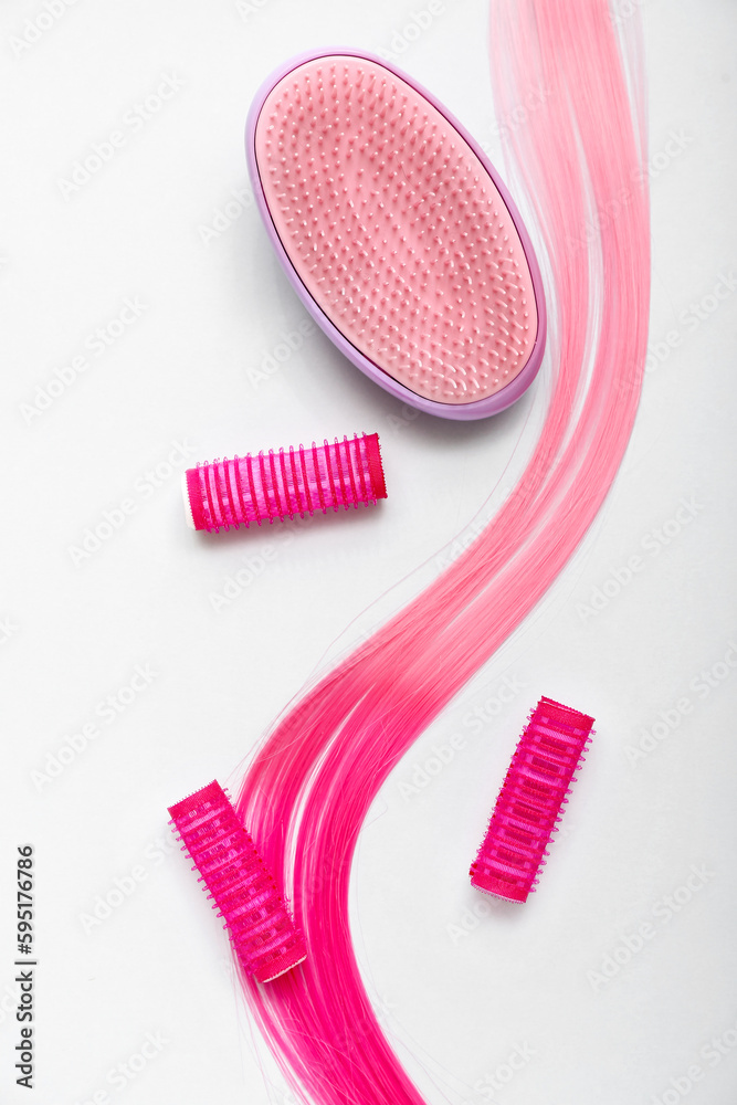 Pink hair strand with curlers and brush on white background