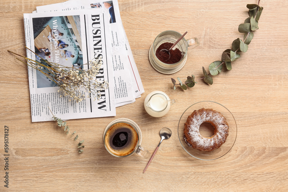 Cup of coffee with milk, cake, newspapers and eucalyptus branches on light wooden background