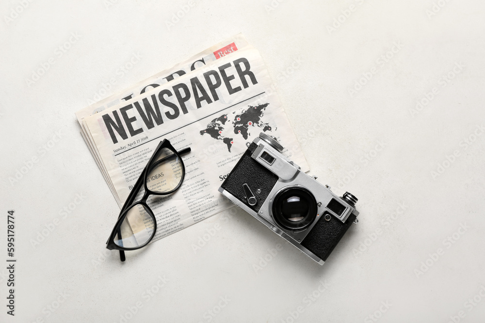 Newspaper with eyeglasses and photo camera on white background