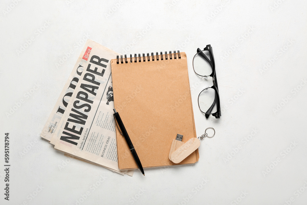 Notebook with USB flash drive, newspapers and eyeglasses on white background