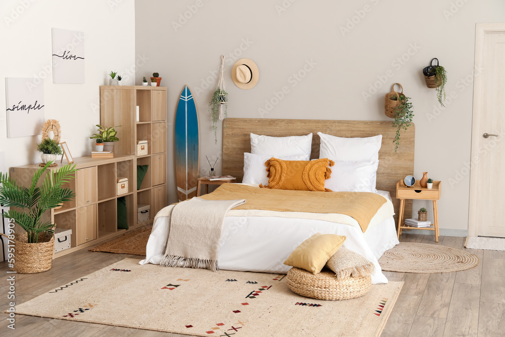 Interior of light bedroom with surfboard, houseplants and shelving unit