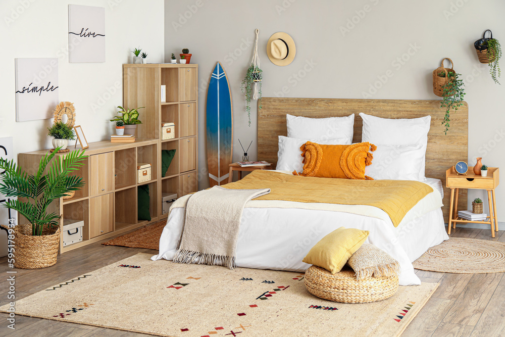 Interior of light bedroom with surfboard, houseplants and shelving unit