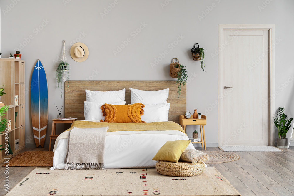 Interior of light bedroom with surfboard, houseplants and big bed