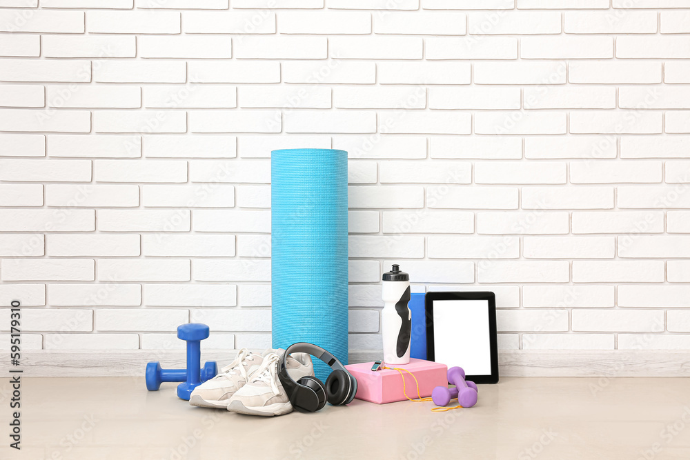 Sports equipment with headphones, tablet computer and bottle near white brick wall