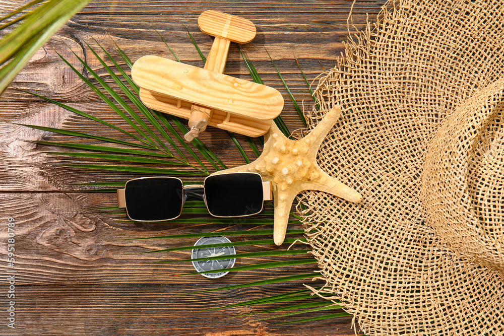 Composition with sunglasses, airplane, starfish, compass and palm leaf on wooden background