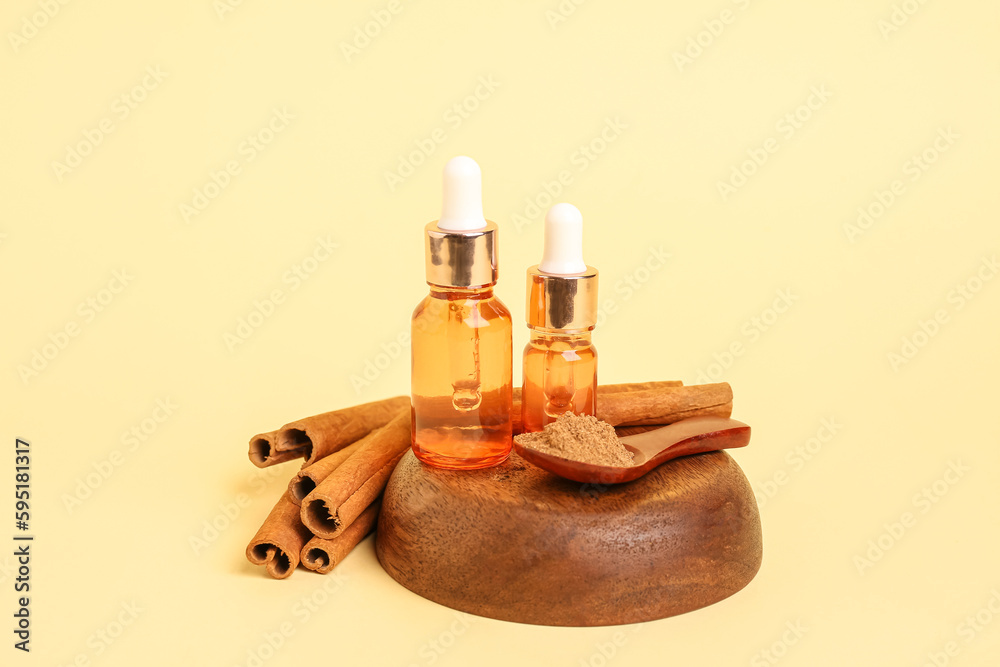 Bowl with bottles of essential oil, cinnamon sticks and powder on yellow background