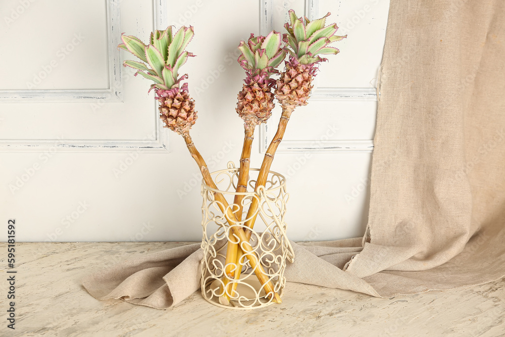 Vase with decorative pineapples on table near light wall