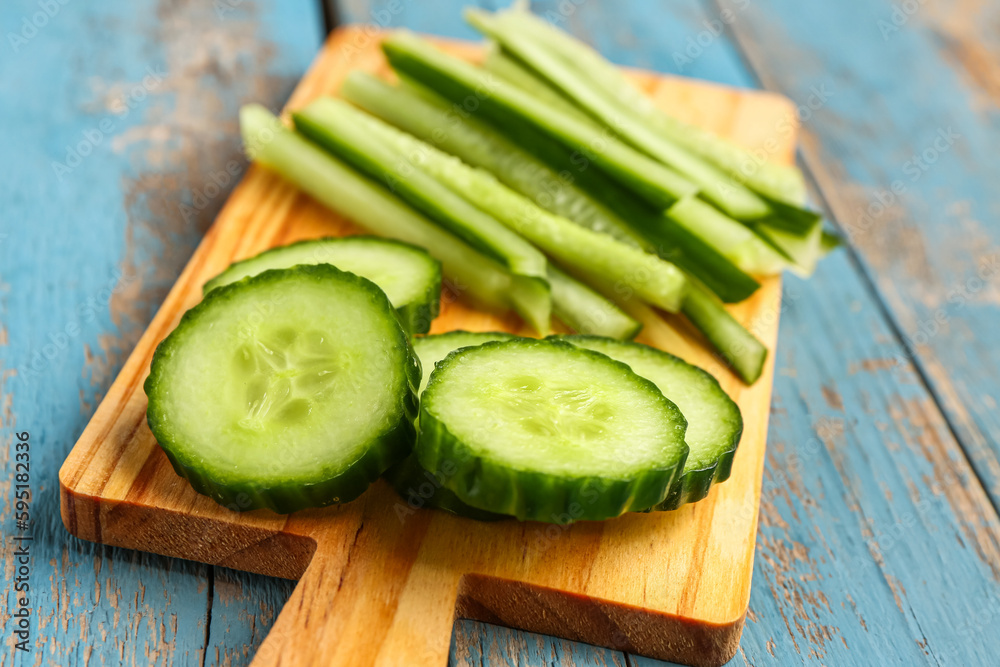 Board with fresh cut cucumber on blue wooden background, closeup