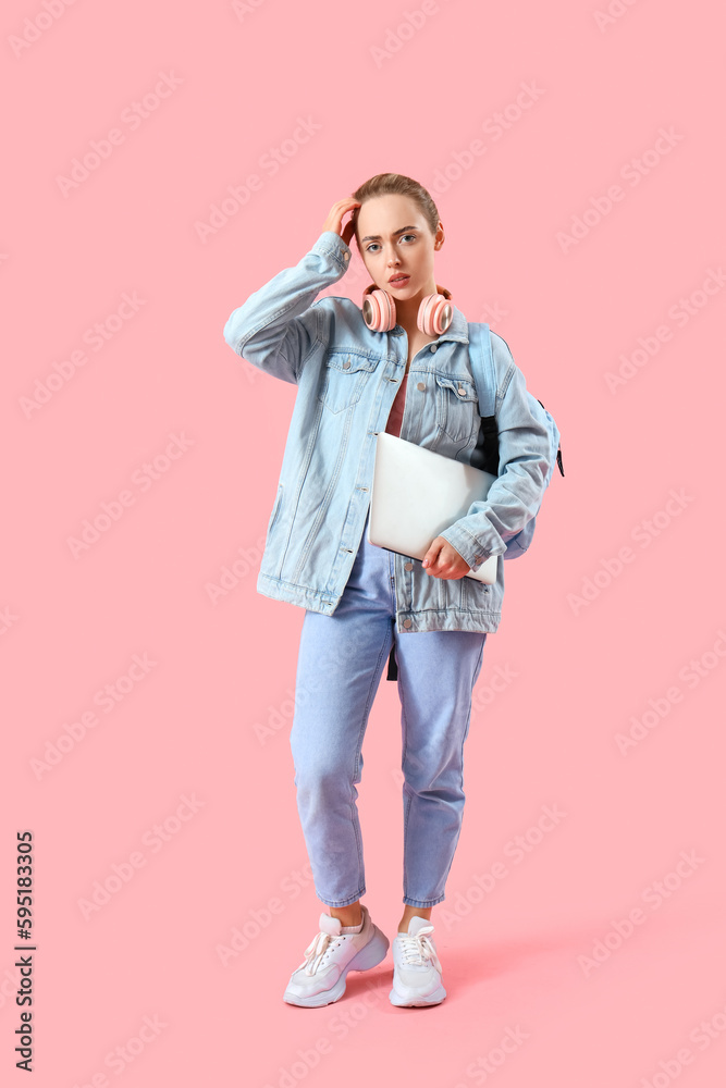 Upset female student with laptop on pink background