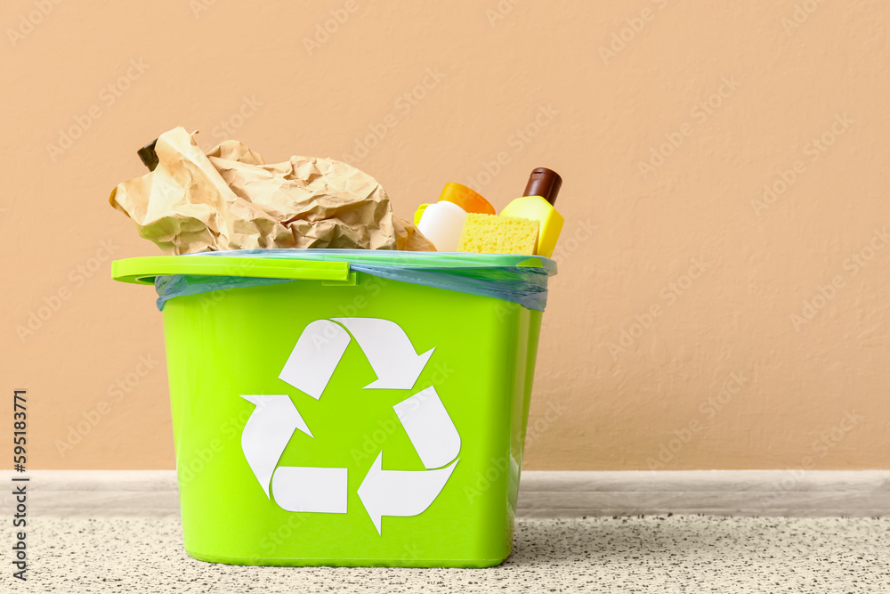 Trash bin with different garbage near beige wall