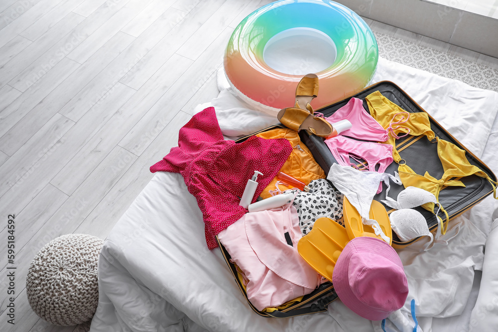 Open suitcase with beach accessories on bed in room