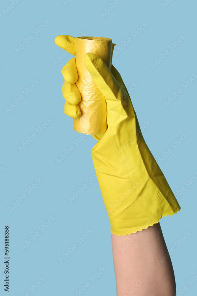 Hand in rubber glove with roll of garbage bags on blue background