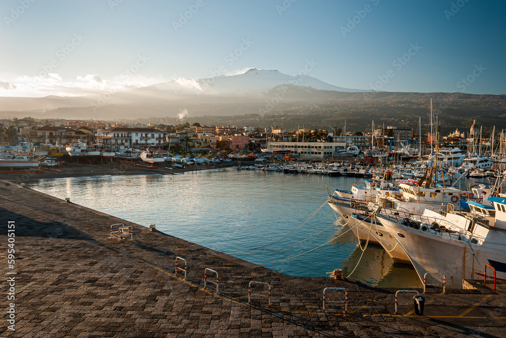 The harbor of Riposto during the sunset; snowy volcano Etna in the background