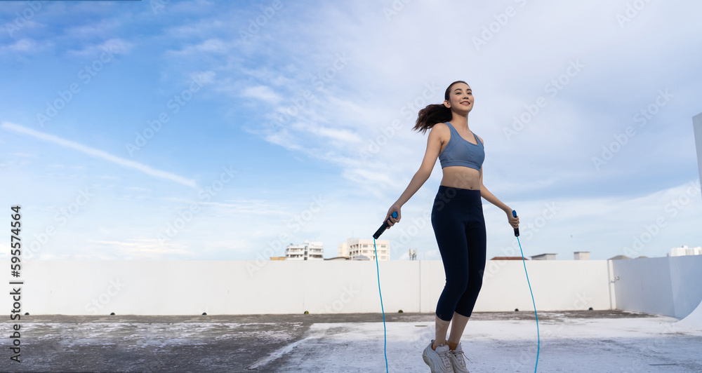 Young Asian woman with jump rope on rooftop. Fitness female doing skipping workout outdoors