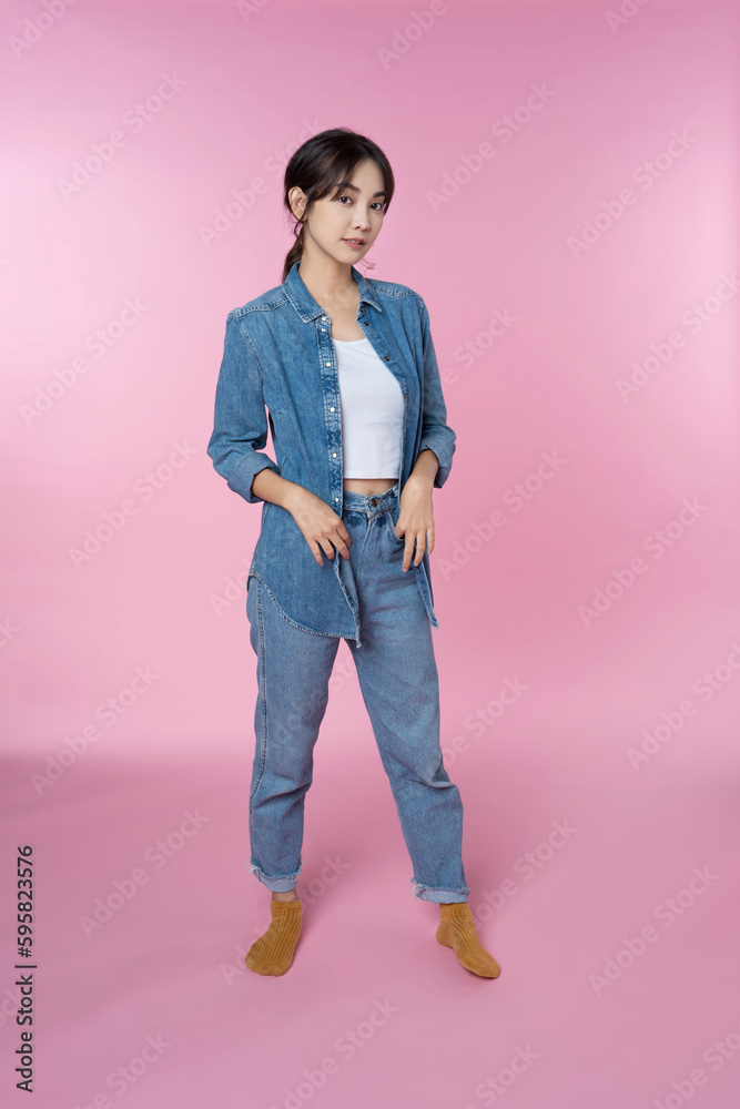 Full length portrait of young beautiful Asian woman in blue jeans jacket isolated over pink backgrou