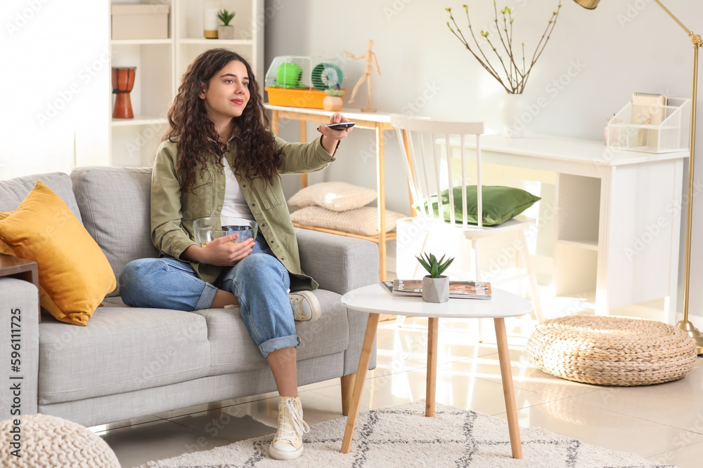 Teenage girl with bowl of chips watching TV at home