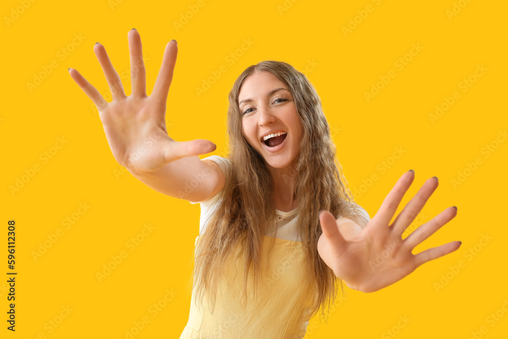 Happy young woman showing hands on yellow background