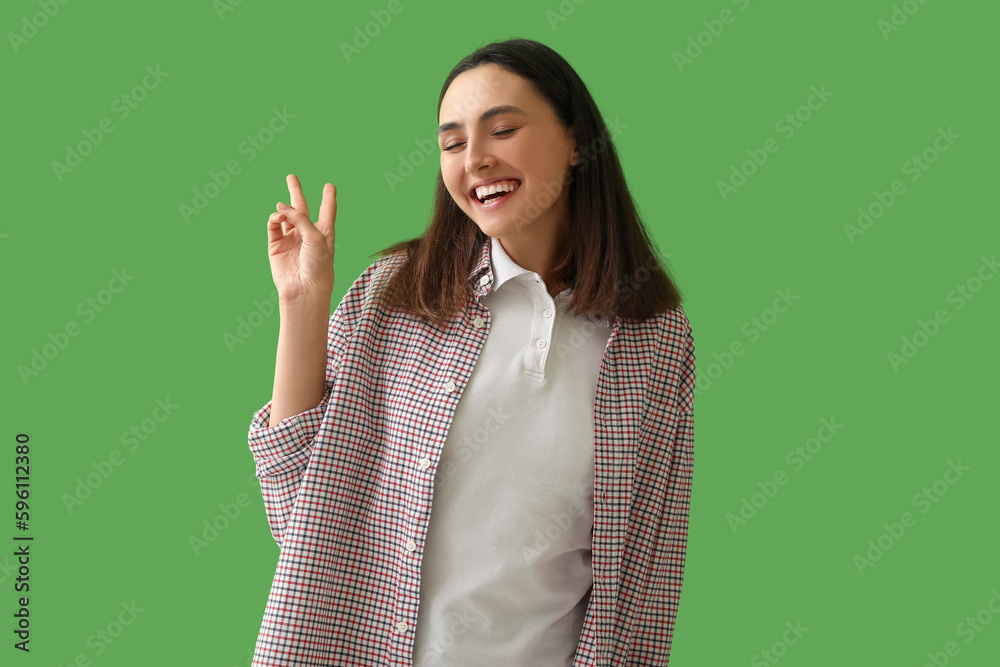 Happy young woman showing victory gesture on green background