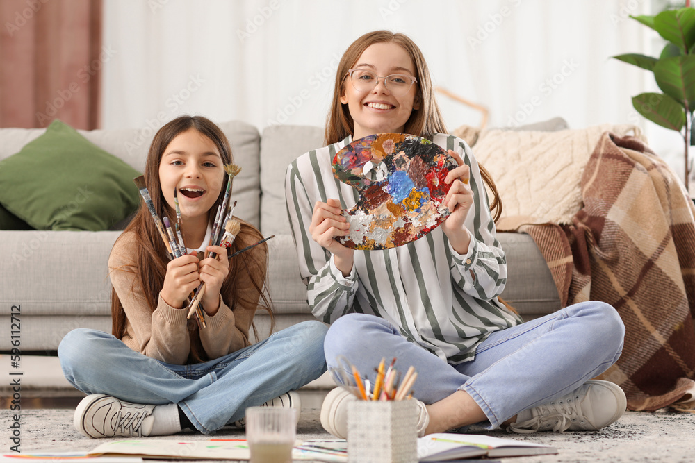 Little girl and her drawing teacher with paint brushes at home