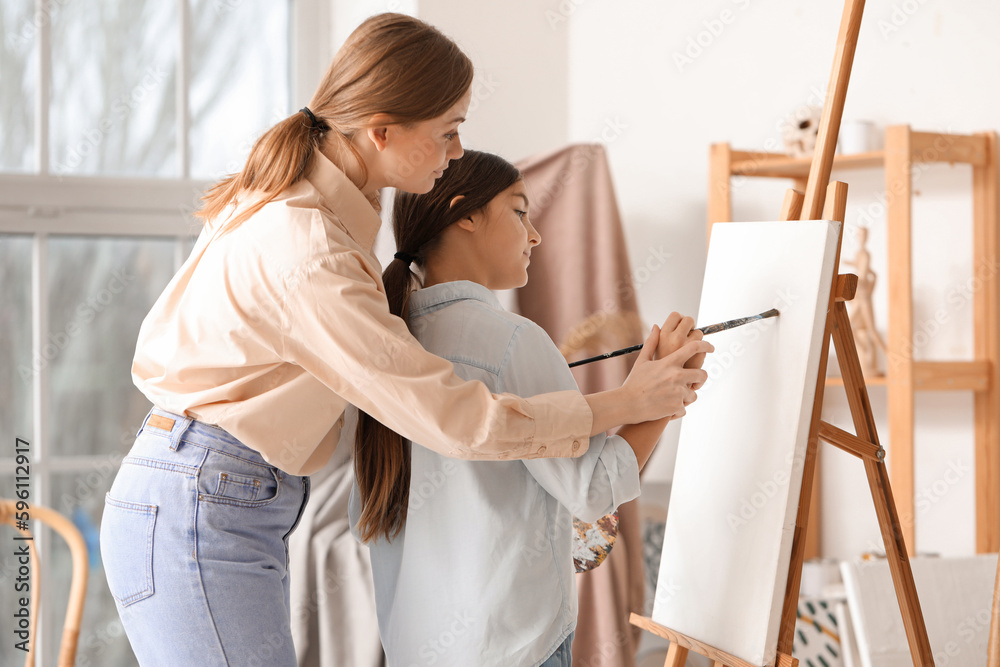 Drawing teacher giving private art lesson to little girl near easel in workshop