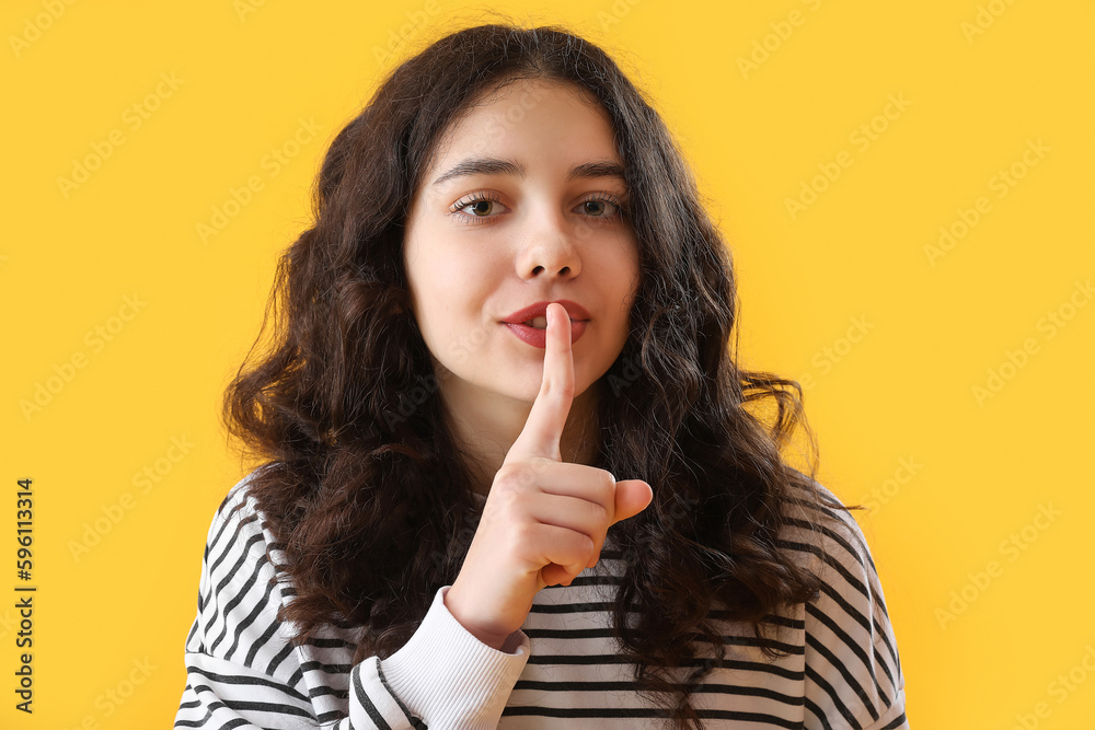 Teenage girl showing silence gesture on yellow background, closeup