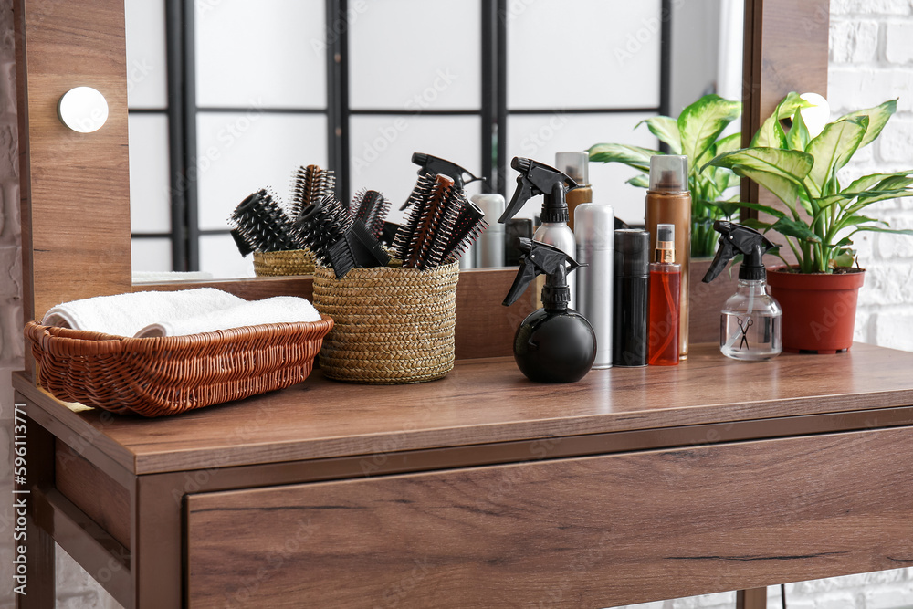 Different hair sprays and brushes on table in beauty salon