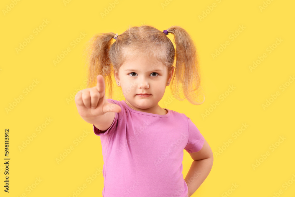 Funny little girl showing loser gesture on yellow background