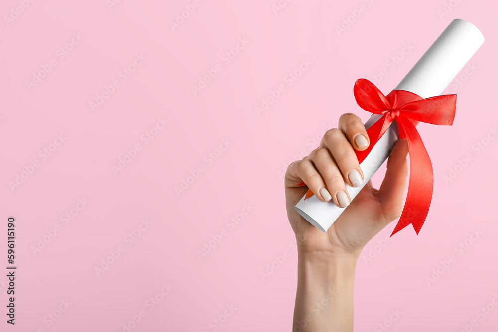 Woman holding diploma with ribbon on pink background