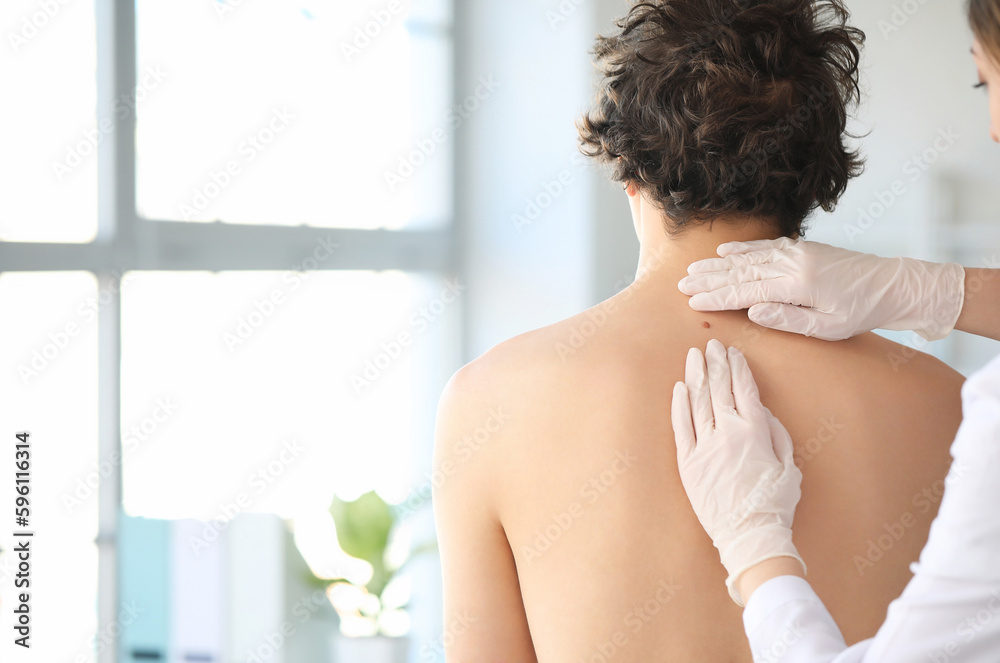 Dermatologist examining mole on young mans back in clinic