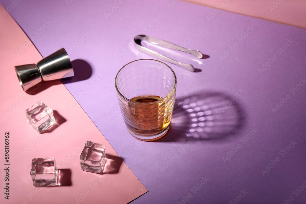 Glass of rum, ice cubes, tongs and jigger on colorful background