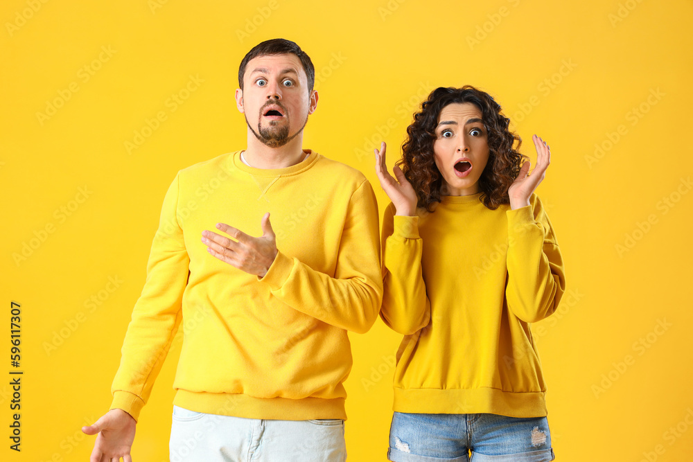 Shocked young couple on yellow background