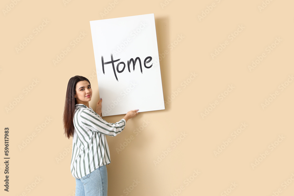 Young woman hanging picture on beige wall