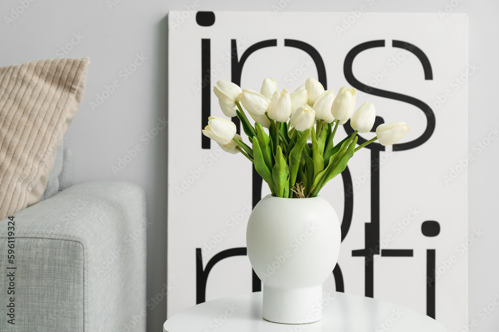 Vase with beautiful tulip flowers on table and poster near grey wall