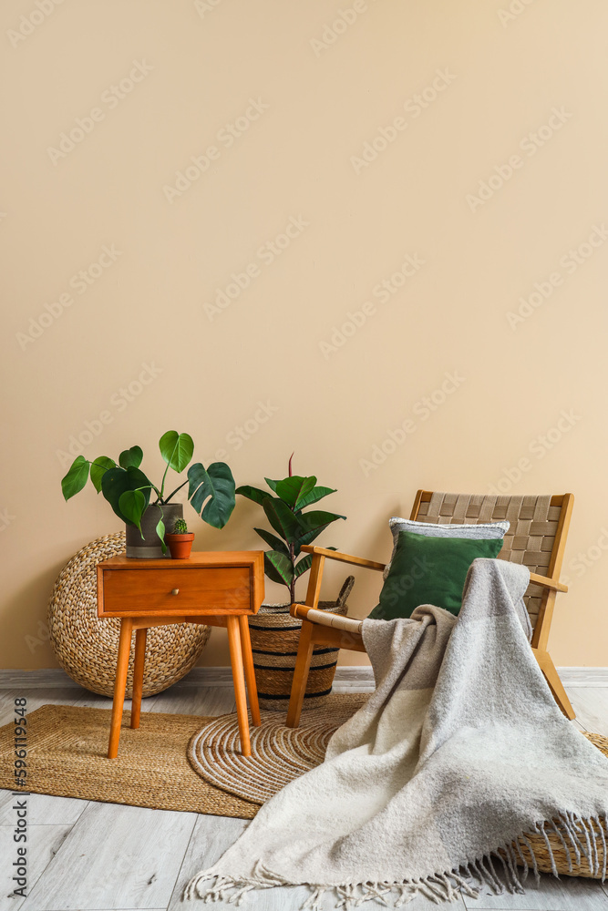 Cozy armchair with cushion, plaid, houseplants and table near beige wall