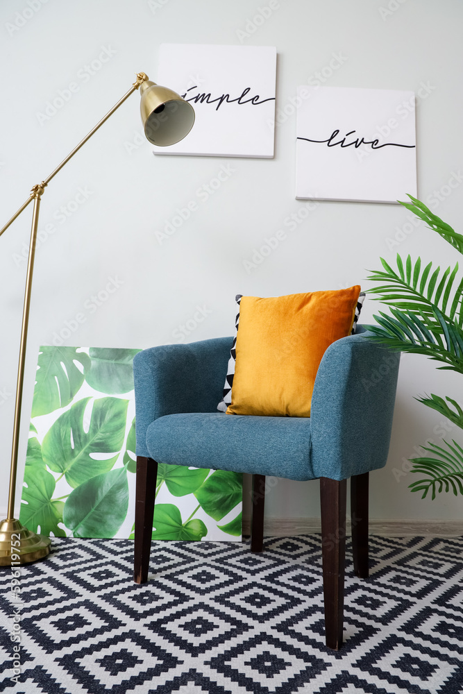 Cozy armchair with cushions, lamp and posters near grey wall