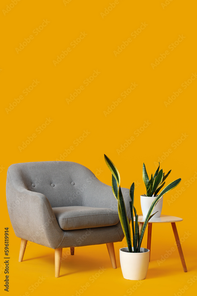 Cozy grey armchair, houseplants and table on orange background