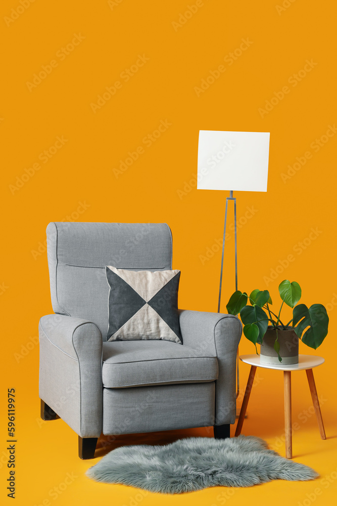 Cozy grey armchair, lamp and table with houseplant on orange background