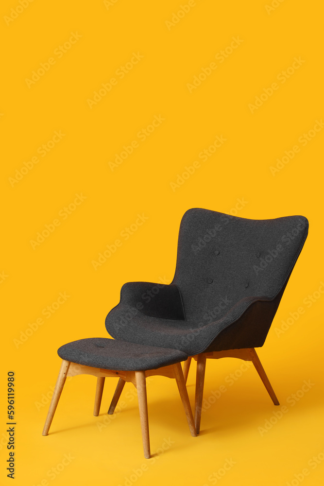 Cozy black armchair with footstool on orange background