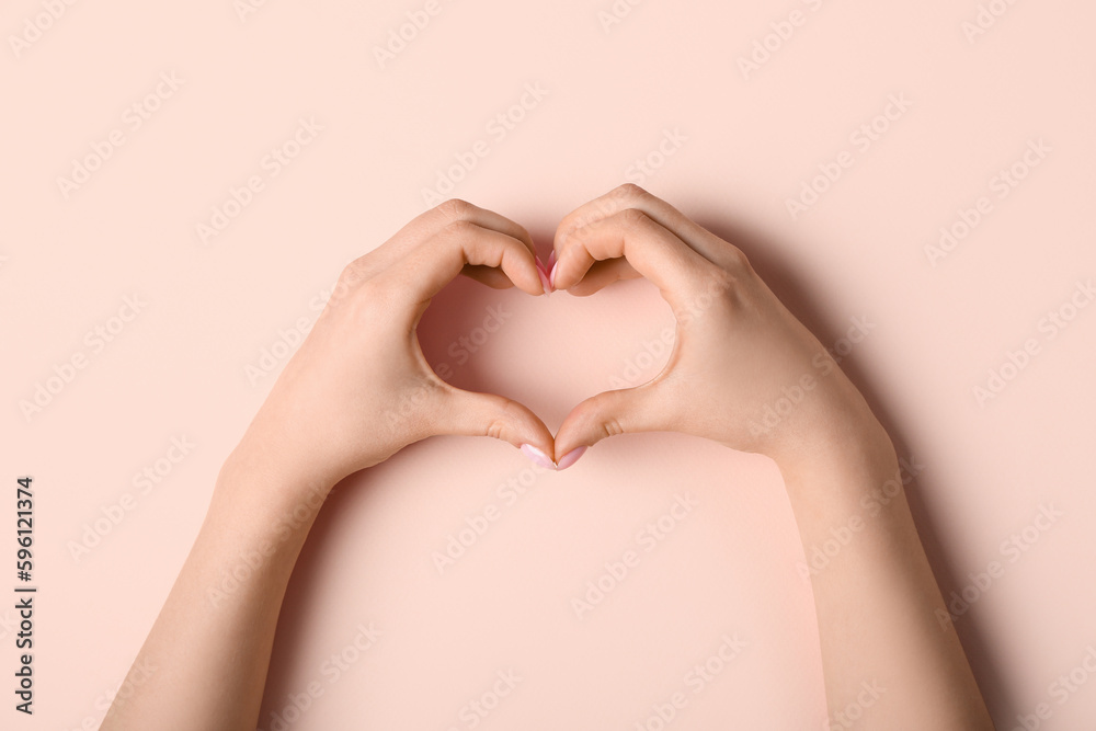 Woman making heart with her hands on beige background