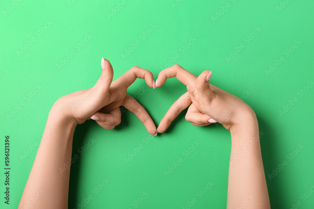 Woman making heart with her hands on green background