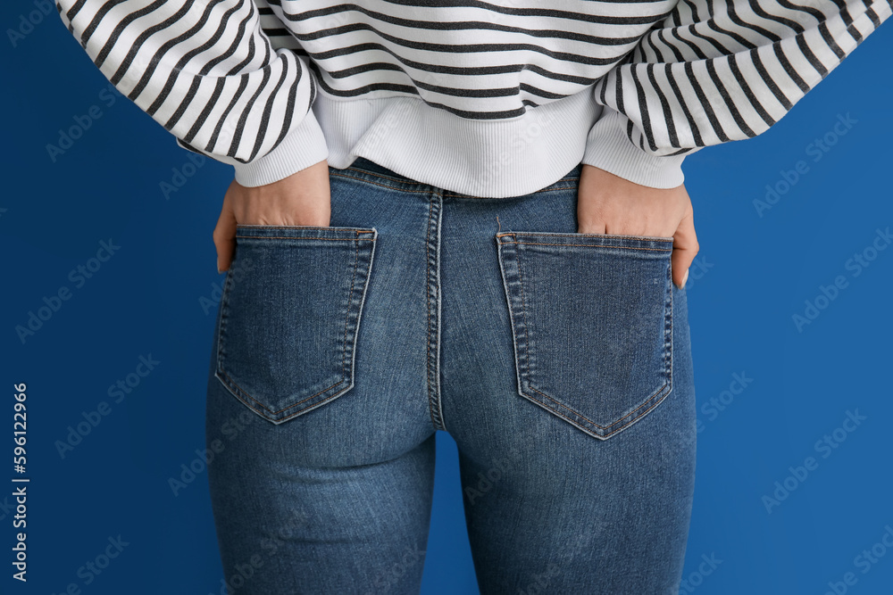 Young woman in stylish jeans on blue background, back view