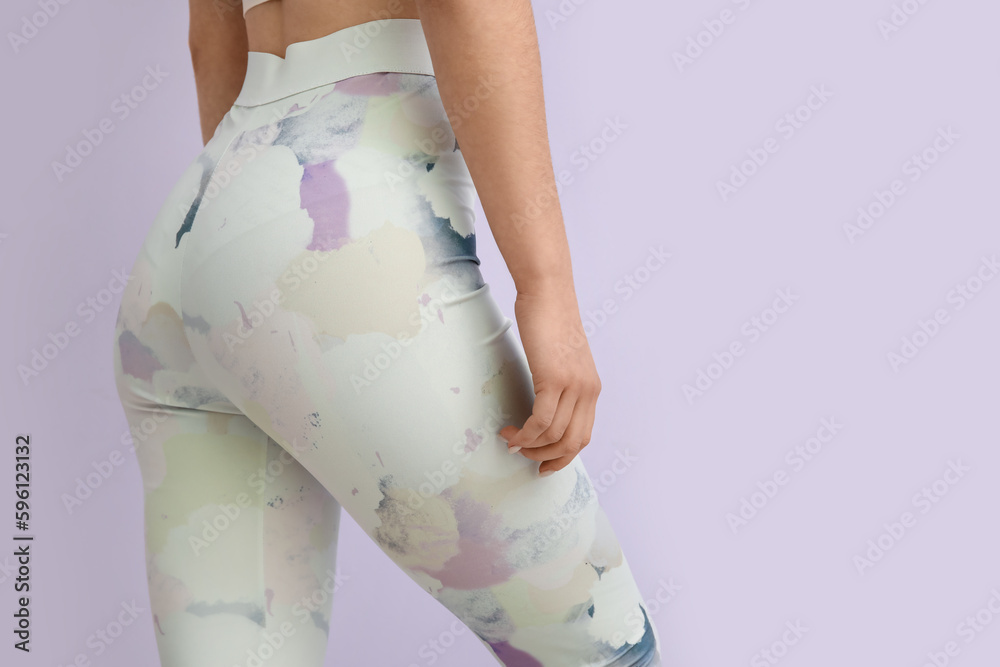 Sporty young woman in leggings on lilac background, closeup