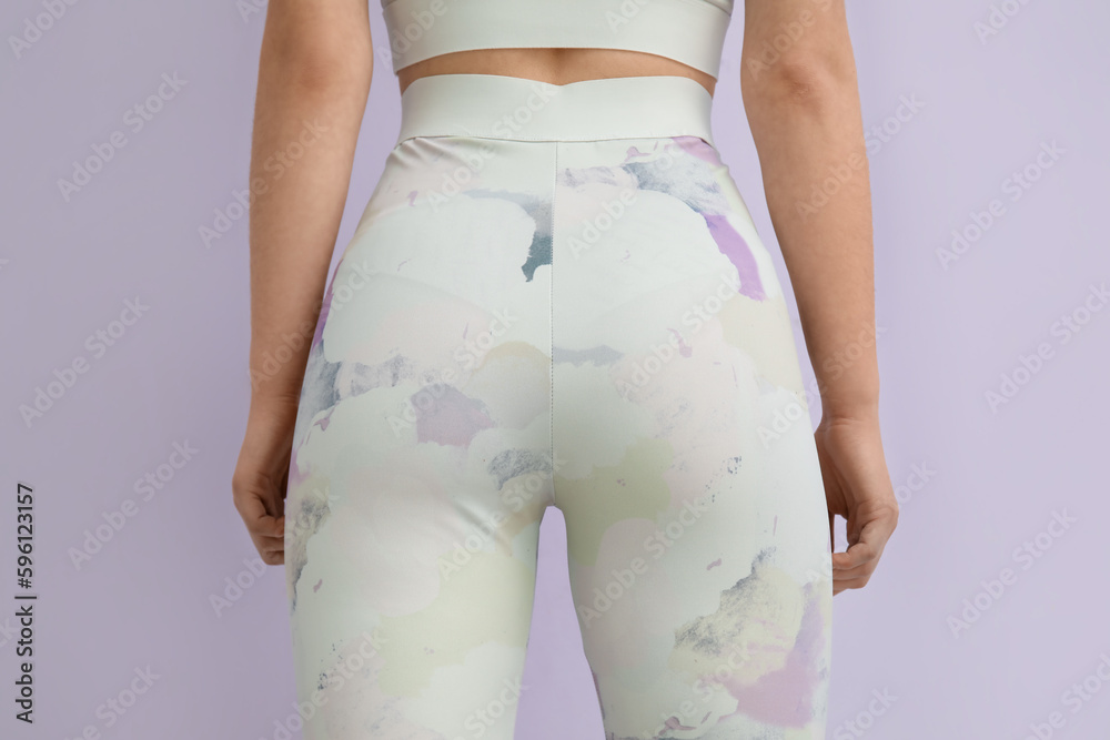 Sporty young woman in leggings on lilac background, back view