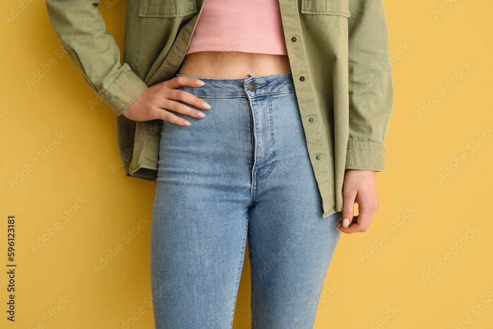 Young woman in stylish jeans on yellow background, closeup