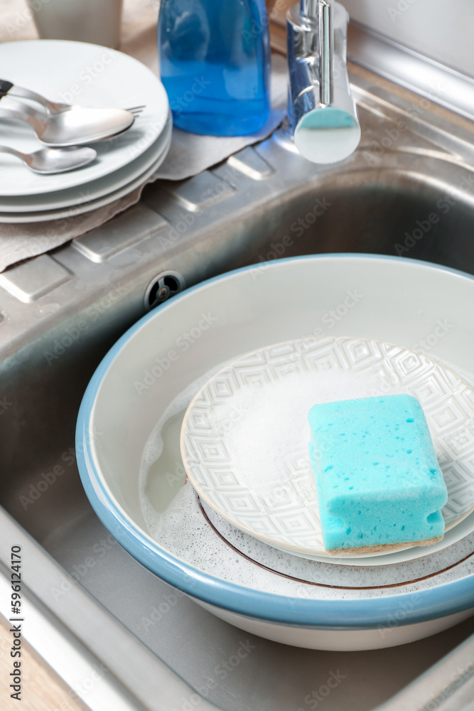 Dishes with cleaning sponge in sink, closeup