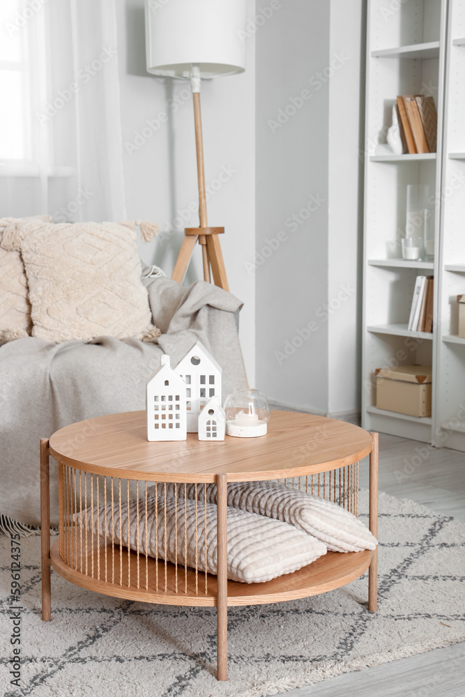 Coffee table with decorative houses and burning candle in interior of living room