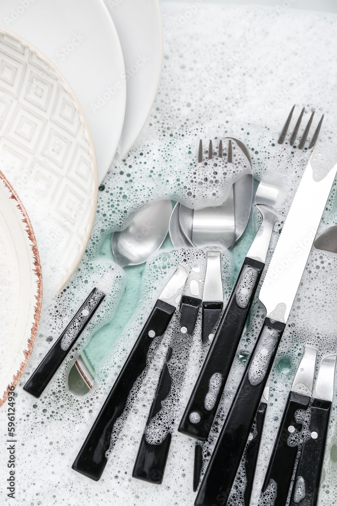 Cutlery with plates and foam in water, closeup