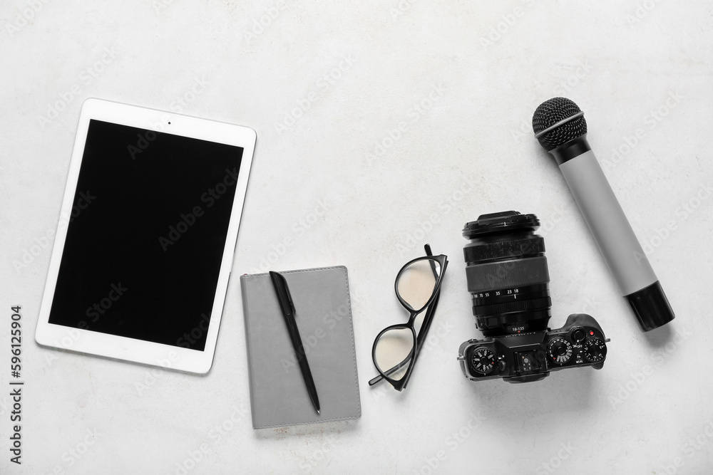 Tablet computer with notebook, eyeglasses, photo camera and microphone on white background